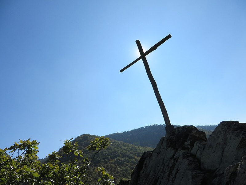 Hier steht ein Bild mit dem Titel: Unbarmherzig brennt die Sonne auf das karges Holzkreuz, das unseren dritten Gipfel markiert (Foto: Hans-Joachim Schneider)